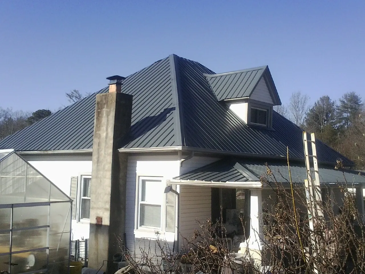 Dark blue standing seam metal roof on a white farmhouse with dormer — Slate & Tile Roof Repair by Roofing Brothers in Shippensburg