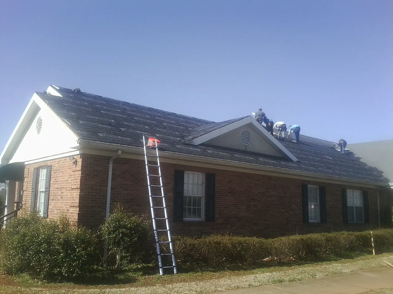 Crew tearing shingles off a brick ranch roof with a ladder set — Metal Roof Repair work by our crew in Shippensburg