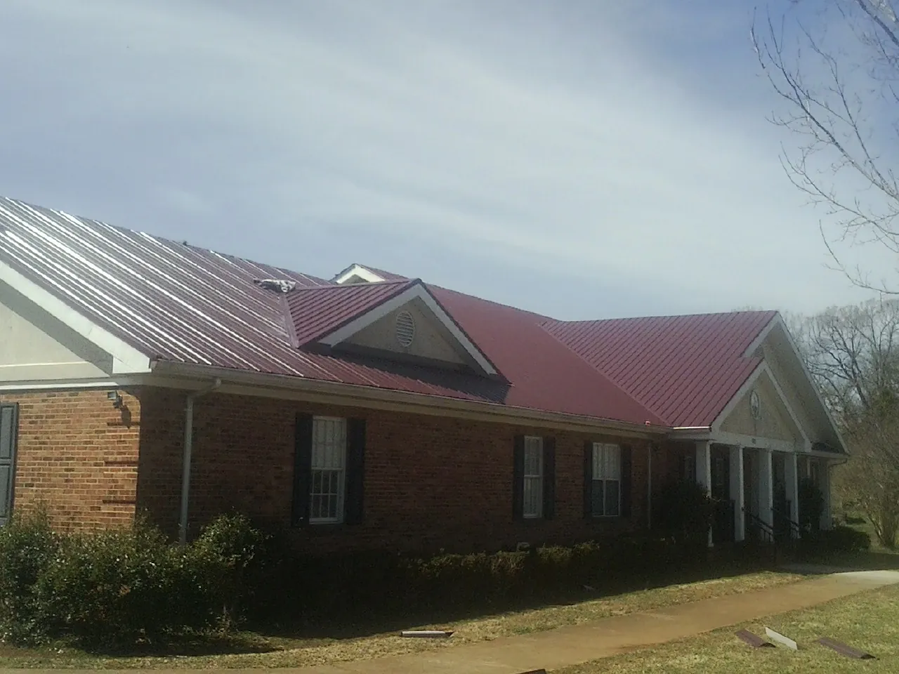 Red metal roof with gabled entries on a long brick building, from a Hail Damage Roof Repair job in Shippensburg