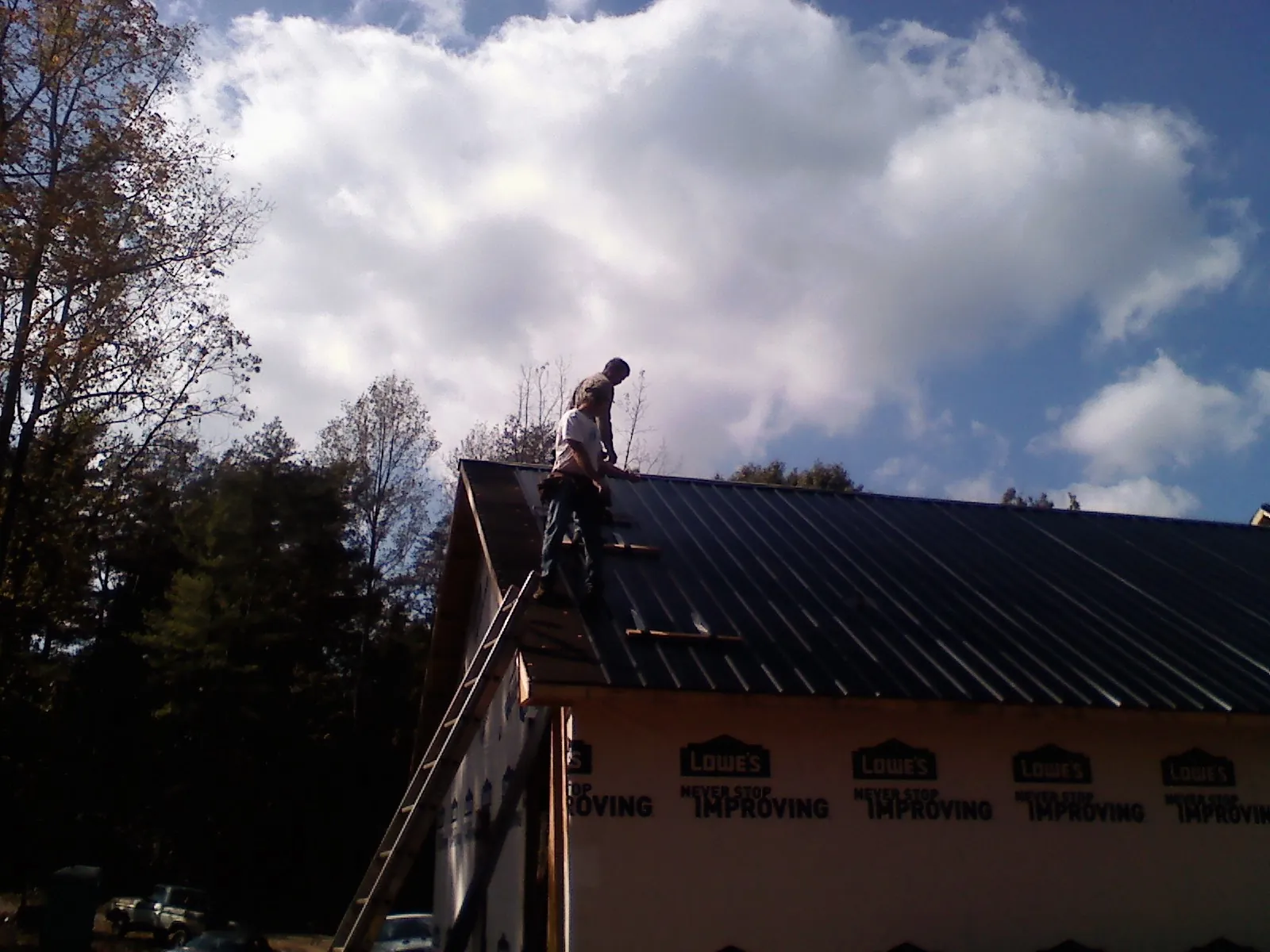 Roofer fastening dark metal panels high against a cloudy sky, from a Roof Inspection job in Shippensburg