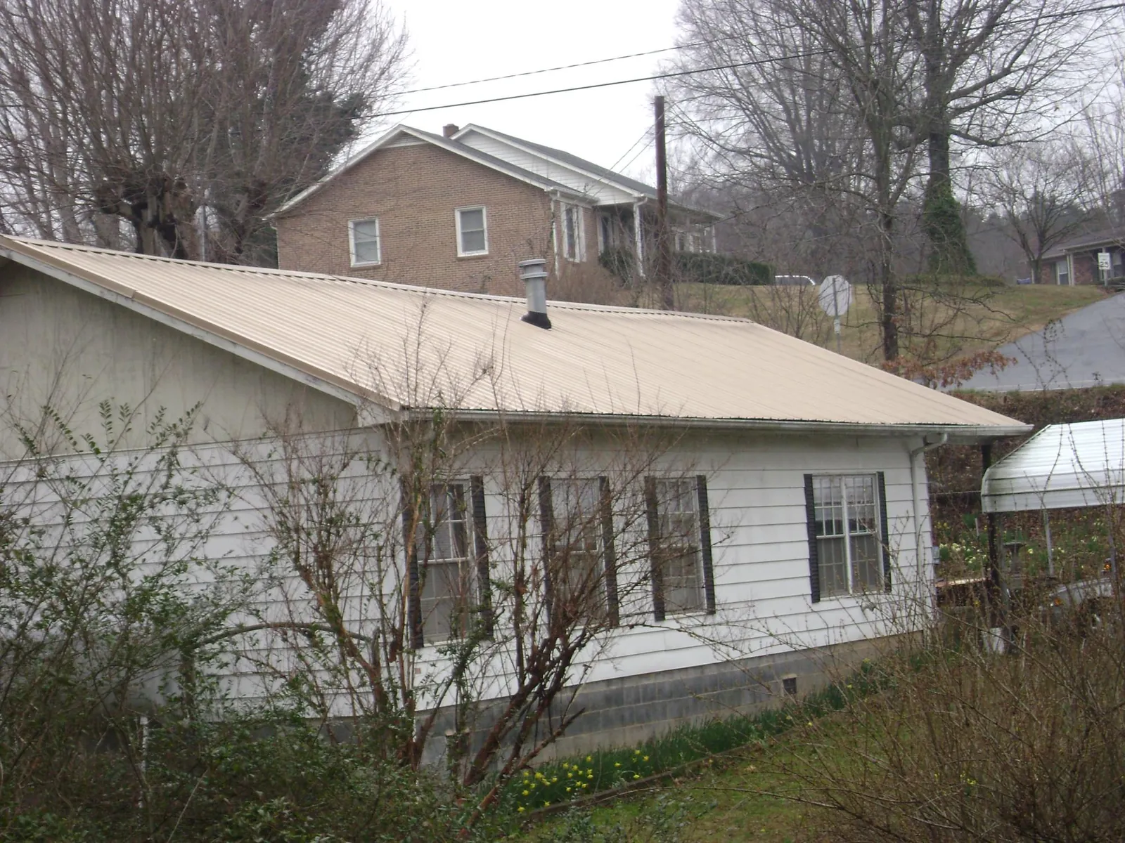 Tan metal roof on a white sided house set into a hillside — Commercial Roofing by Roofing Brothers in Shippensburg
